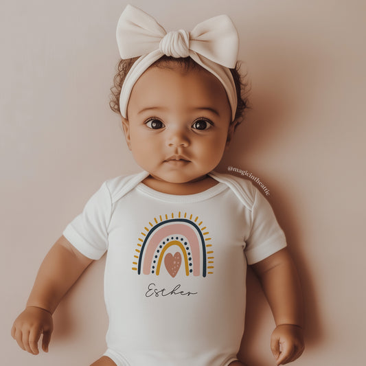 Bebé vistiendo body con diseño de arcoíris. Personalizable con el nombre del bebé.
