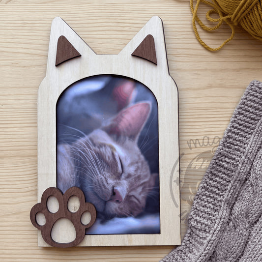 Marco de fotos con forma de gato en madera vista cenital sobre mesa de madera clara junto a manta y ovillo de lana