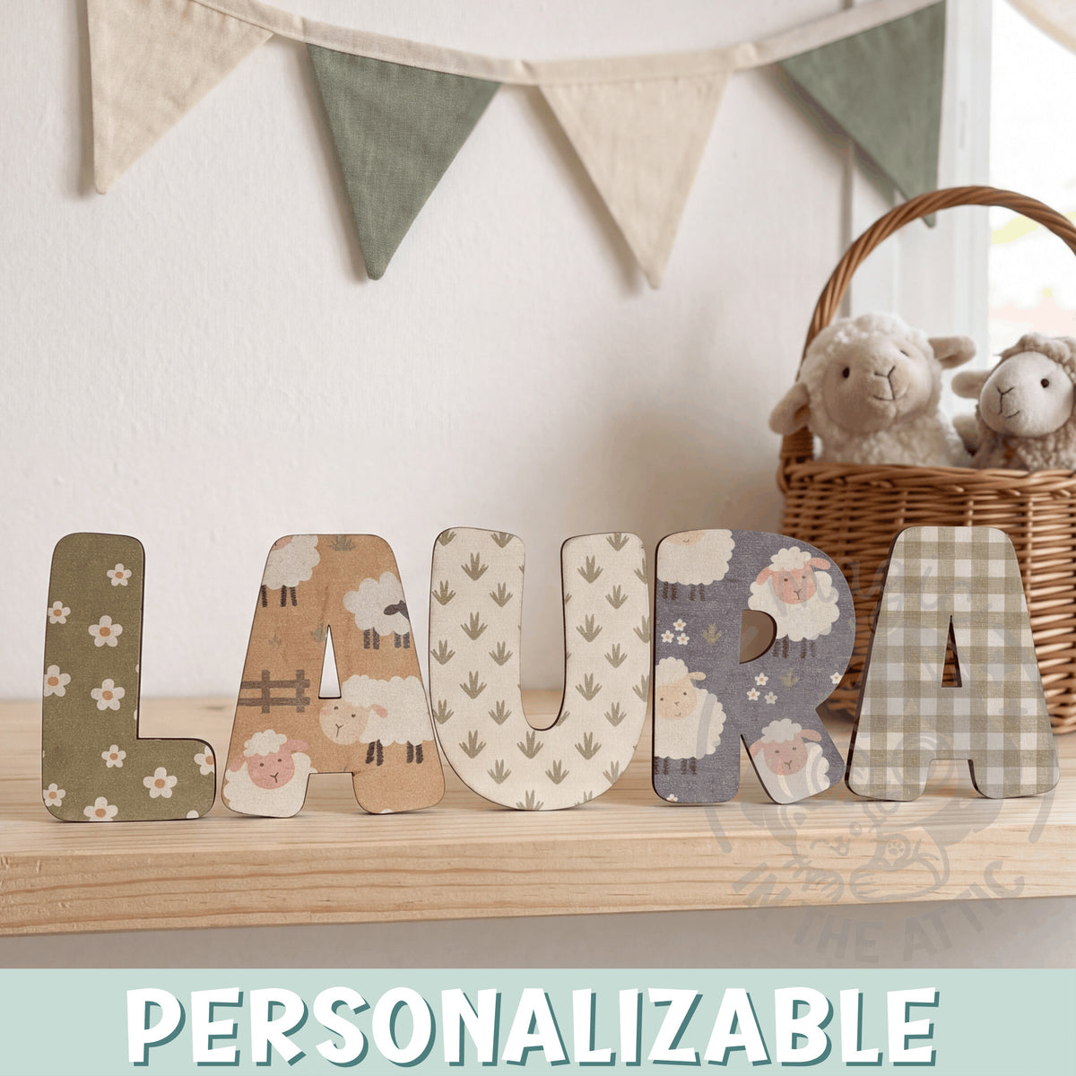 Letras de madera personalizadas con estampado de ovejitas y flores formando el nombre Laura, sobre balda de madera clara en habitación infantil