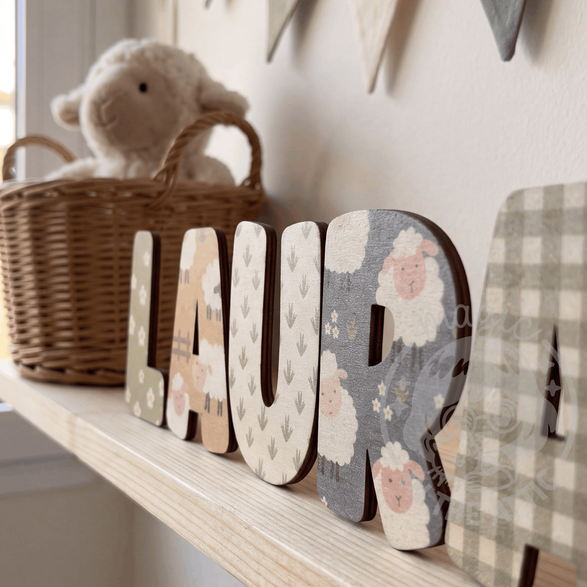 Letras de madera personalizadas con estampado de ovejitas y flores formando el nombre Laura, sobre balda de madera clara en habitación infantil