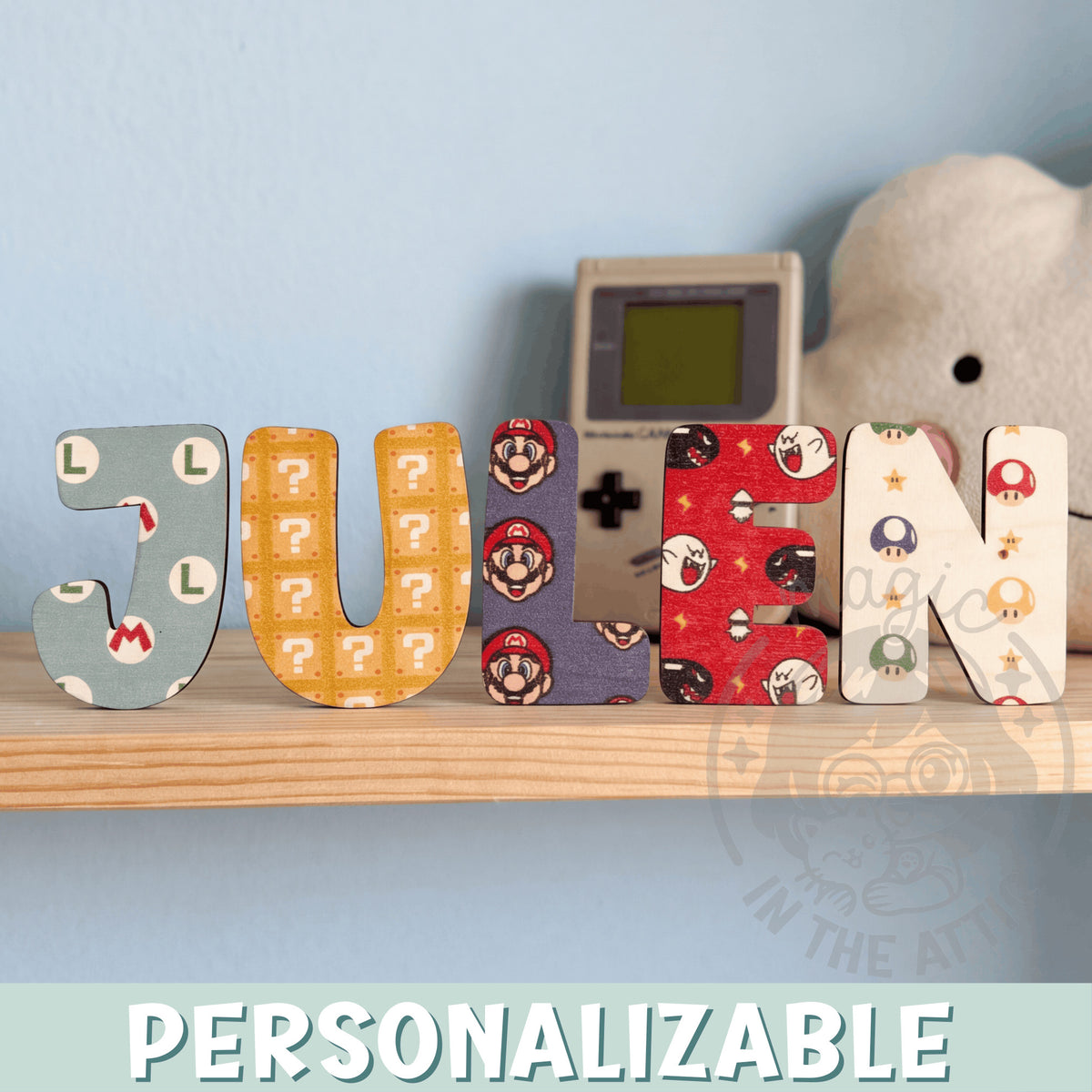 Letras de madera personalizadas con estampado de Super Mario formando el nombre Julen, sobre balda de madera clara junto a pared azul