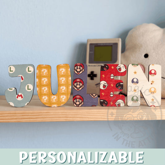 Letras de madera personalizadas con estampado de Super Mario formando el nombre Julen, sobre balda de madera clara junto a pared azul