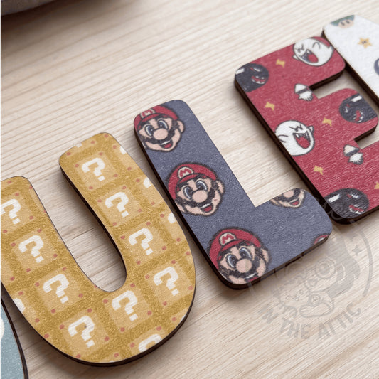 Letras decorativas de madera con nombre personalizado y motivo de Super Mario en vista cenital sobre superficie de madera clara