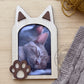 Marco de fotos con forma de gato en madera vista cenital sobre mesa de madera clara junto a manta y ovillo de lana
