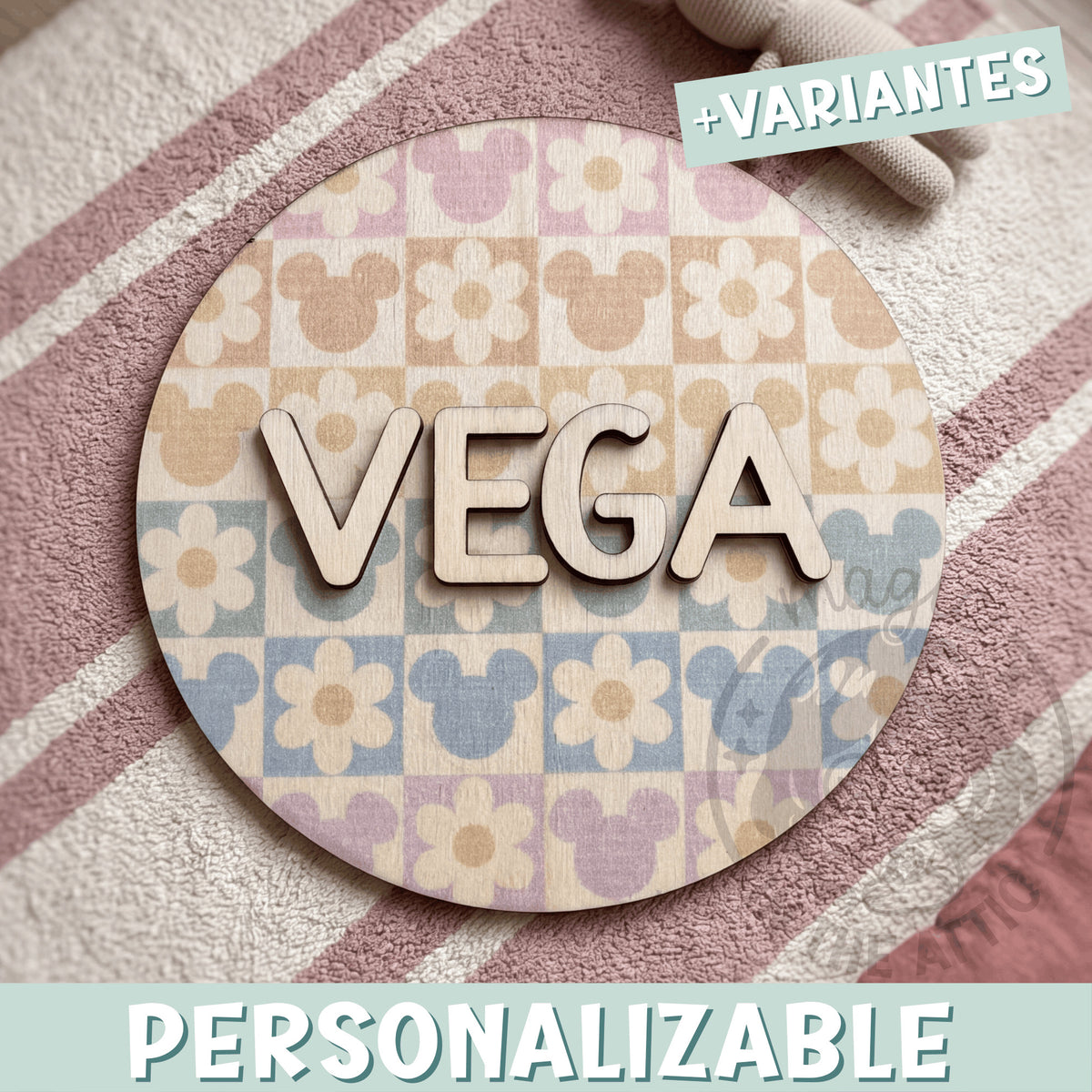 Placa de madera redonda personalizada con el nombre Vega en letras de madera natural en relieve, sobre un fondo impreso de cuadros pastel con flores y siluetas de Mickey, encima de una alfombra de rayas rosas
