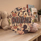 Placa de madera redonda con el nombre Queralt y estampado de Mickey y sus amigos, apoyada en una cómoda junto a un conejito de peluche y unos libros infantiles