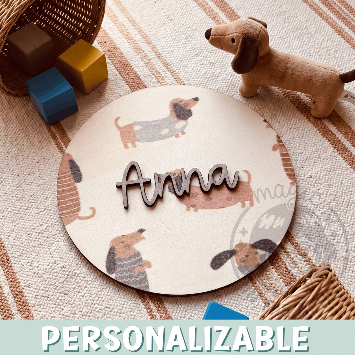 Placa de madera redonda personalizada con el nombre Anna en letras de madera oscura en relieve, sobre un fondo impreso de perritos salchicha con jersey en tonos tierra, encima de una alfombra de rayas junto a un perro de peluche y bloques de madera de colores