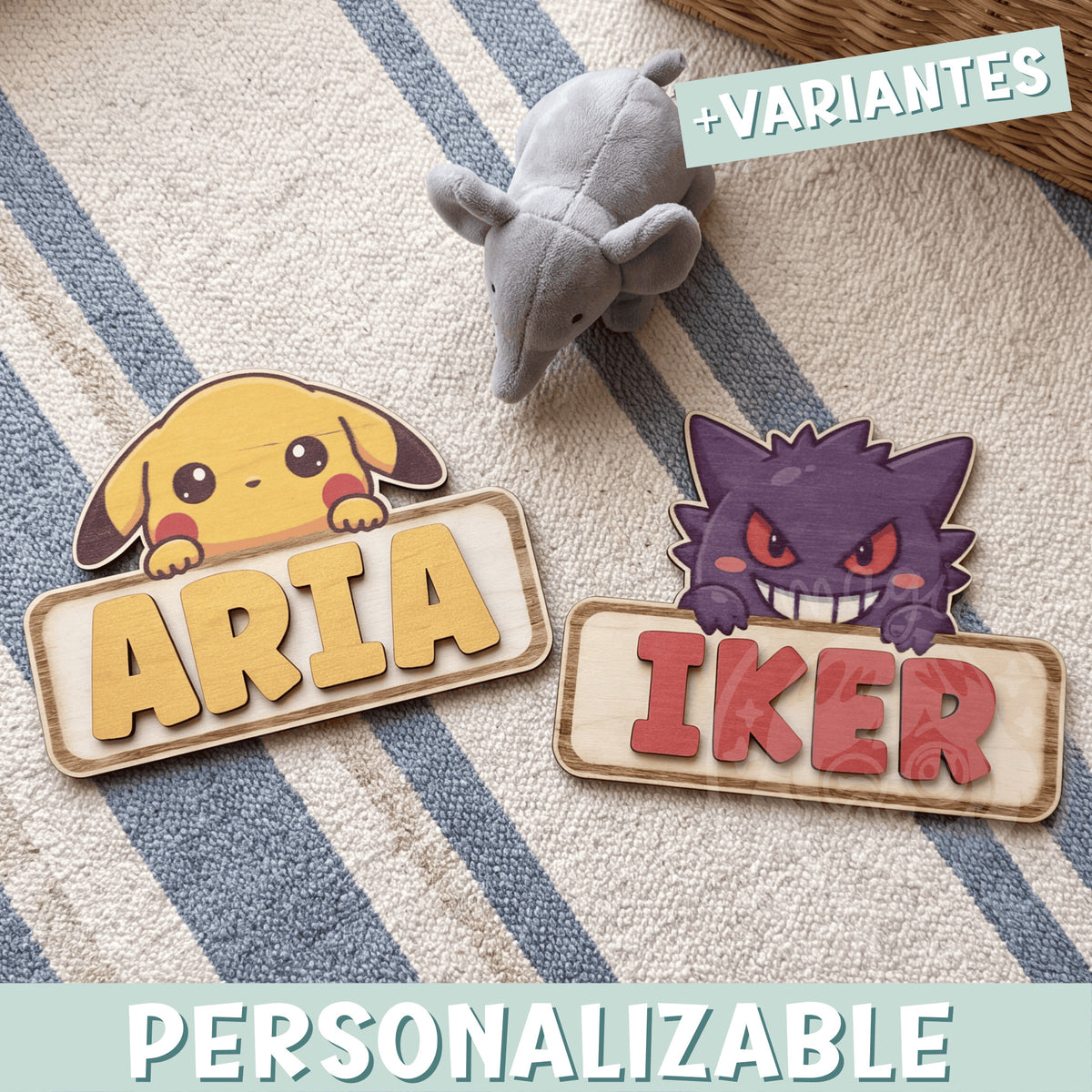 Dos placas de madera personalizadas con nombre y un Pokémon asomando por encima: Pikachu con el nombre Aria en letras amarillas y Gengar con el nombre Iker en letras rojas, sobre una alfombra de rayas azules junto a un peluche gris