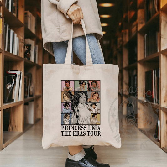 Tote bag de algodón color crudo con collage de ilustraciones de la Princesa Leia de Star Wars en sus distintas épocas sobre fondos de colores pastel, con el texto “Princess Leia – The Eras Tour”, llevada en la mano por una persona en una biblioteca.
